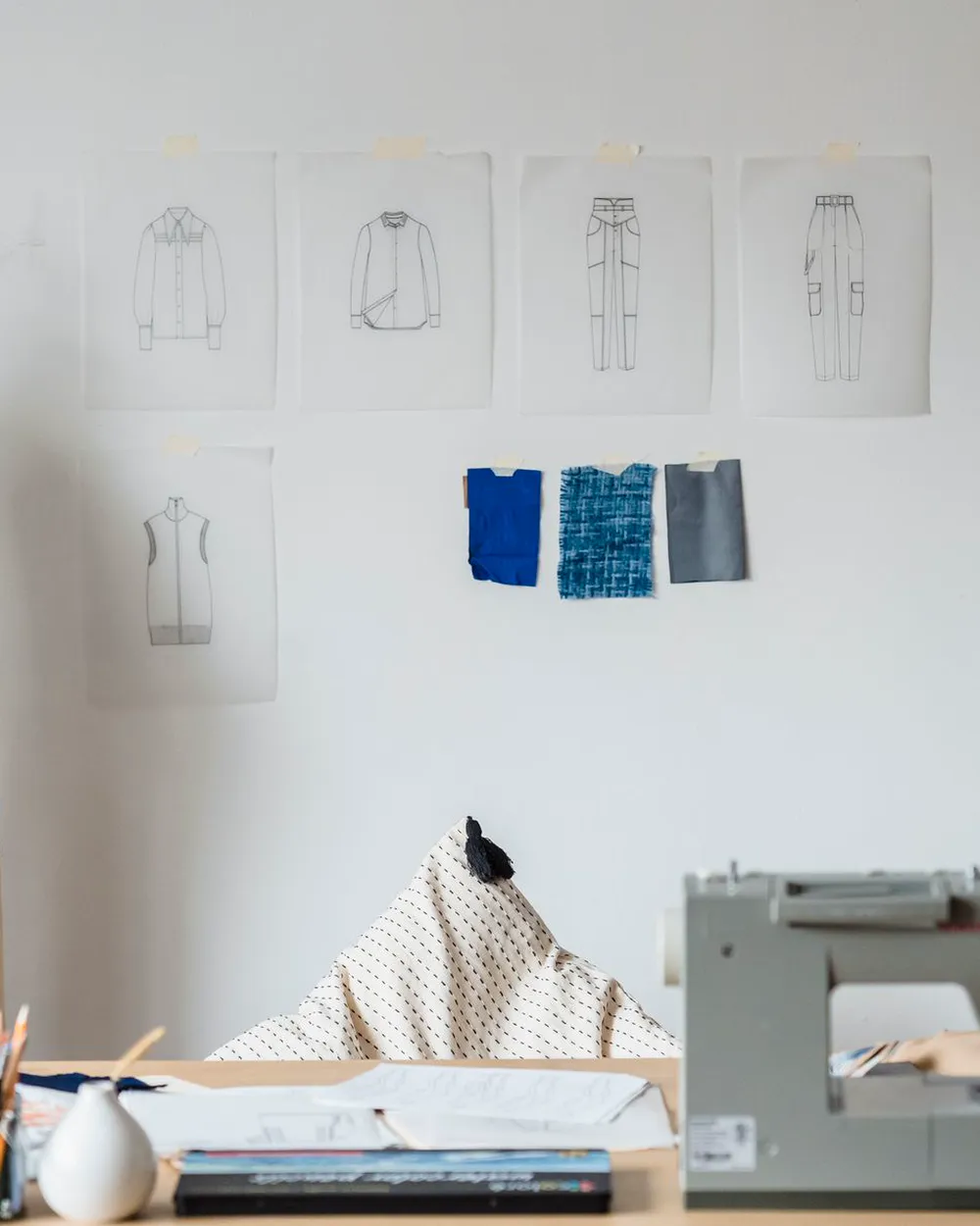 The atelier: a sewing machine beneath a wall of sketches